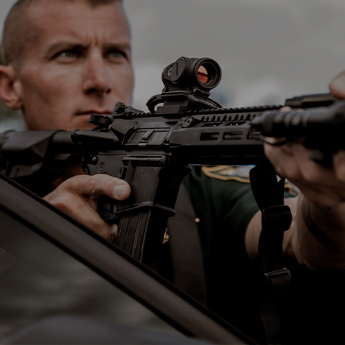 Active-Duty LE: Tactical police officer aiming a rifle with a DUTY RDS (Red Dot Sight).